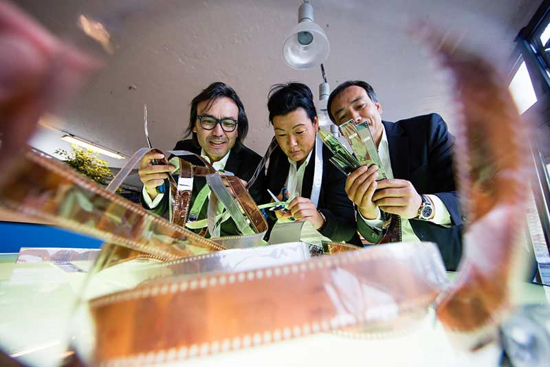 Drei Mitarbeiter bearbeiten Filmstreifen und Negative in einem hellen Arbeitsumfeld – Business Portraits, Menschen bei der Arbeit.