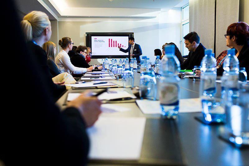 Ein Redner präsentiert bei einem Business-Meeting in Berlin, umgeben von konzentrierten Teilnehmern.